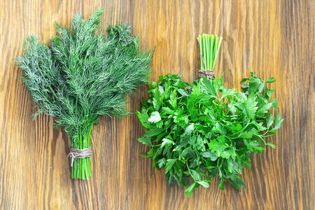 Two bunches of green parsley and dill in in yin and yang position on textured wooden brown background. Horizontal. Top view. Fresh spices from garden, Vegan ingredient and healthy foodの写真素材