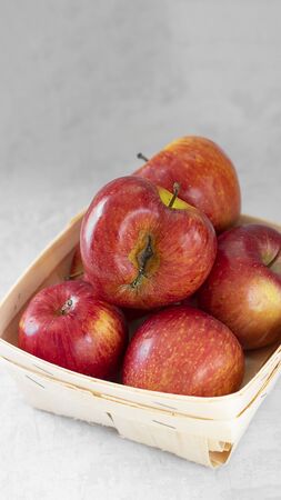 Red fresh organic apples in small wooden pottle with ugly fruit on top. On grey cement background. Buying imperfect product to reduce waste. Sustainable consumption. Vertical banner. Eco trend.の写真素材