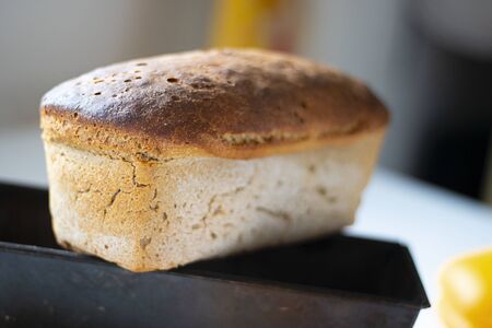 Freshly baked crusty loaf of homemade premium rye and wheat flour bread is getting cold on black metal form. Baking at home using sour dough. Horizontal closeup. Selective focus.の写真素材