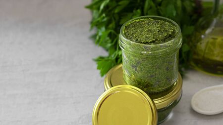 homemade pesto with cashew nuts in glass jar with mockup lug lid, green leaves of spicy herbs and olive oil on background. Vegan, healthy sauce, Italian cuisine. Horizontal banner with copy space.の写真素材