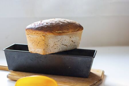 Freshly baked crusty loaf of homemade premium rye and wheat flour bread is getting cold on black metal form on table. Baking at home using sour dough. Selective focus. Horizontal with copy space.の写真素材