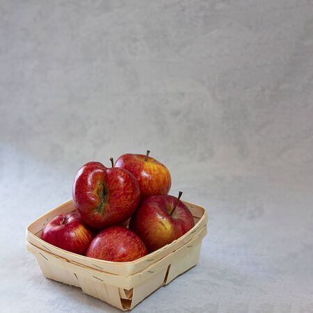 Red fresh organic apples in small wooden pottle with ugly fruit on top. On grey cement background with copy space. Buying imperfect product to reduce waste. Sustainable consumption. Square. Eco trend.の写真素材