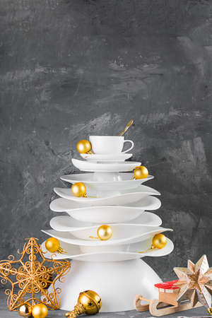 Ceramic white dishes Christmas tree with yellow gold Xmas balls and decoration on dark background. Creative concept, postcard about food, restaurant, menu, party, dishware. Vertical.の写真素材