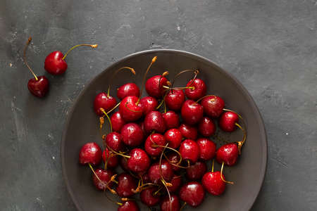 Many ripe bright Cherry with water drops on brown bowl and two berries next to it on dark chalkboard background. Fresh sweet ingredient for desserts, tarts and pies. Organic agriculture. Horizontal.の写真素材