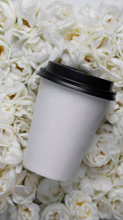 Mockup paper coffee cup on background of Live wall made up with white wild roses. Top view. Full bloom, monochrome flora design. Trendy flower carpet. Hot drink take away. Vertical bannerの写真素材