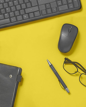 Bright office desk with keyboard, mockup mouse, glasses, notebook with leather cover, pen. Vertical...
