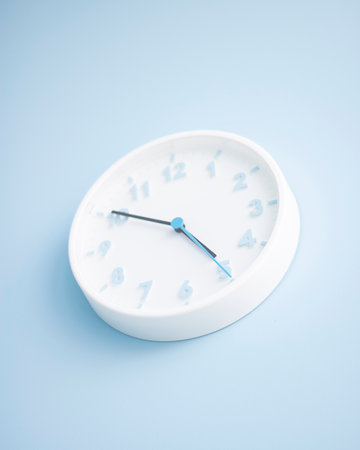 Minimalistic white wall clock on a blue background. Time concept. Vertical with copy space.の写真素材