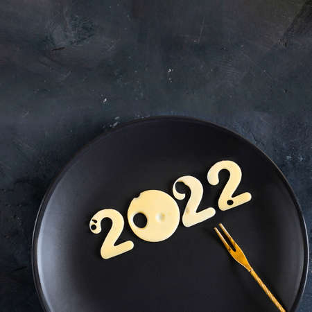 Christmas and New year concept of 2022. Minimal logo for period of time with light cheese snack on fork on plate. Ready picture for postcard with copy space for text and design.の写真素材