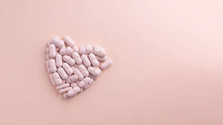 Heart made of pills on pink background. Creative concept for Valentines Day or Pharmacy, Dietary Supplement and Cardio Medicines.の写真素材