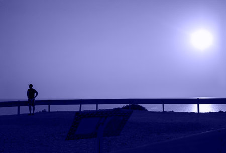 Toned with Very Peri color Bright sunset over the sea and road, traffic devider and dark silhouette of man with cap on his head ,, Horizontal. Mideterranian, cyprus, road, ecology. With copy spaceの写真素材