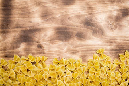 raw Farfalle lie at the bottom of the frame on a wooden table top view with free space at the top of the pictureの写真素材