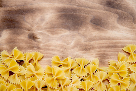 raw Farfalle lie at the bottom of the frame on a wooden table top view with free space at the top of...