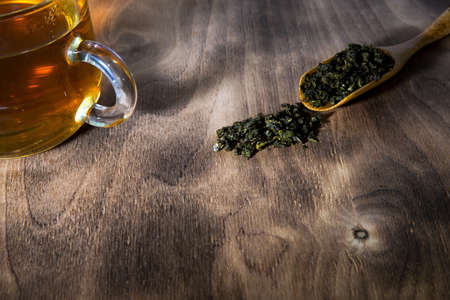cup of green tea and spoon of dried green tea leaves on wooden backgroundの写真素材