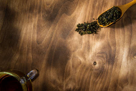cup of green tea and spoon of dried green tea leaves on wooden backgroundの写真素材