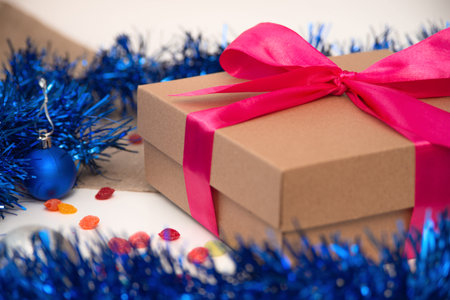 Brown gift box tied with pink ribbon close up on white grey background with silver beads Christmas...