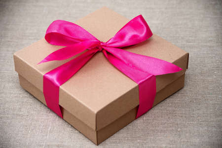 Gift box wrapped in brown recycled paper with pink ribbon on gray backgroundの写真素材
