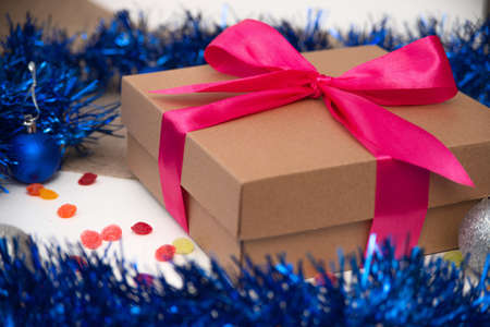 Brown gift box tied with pink ribbon close up on white grey background with silver beads Christmas balls and bellsの写真素材