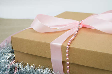 Brown gift box tied with pink ribbon close up on white background, with pink beads and silver bellsの写真素材