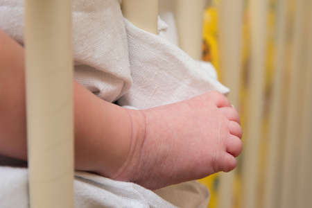 The leg, heel of a sleeping child stuck out from a blanket from a baby cribの写真素材