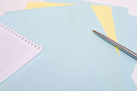 ballpoint pen lies on sheets of blue and yellow paper next to the notebook, white background, layout, Flatleyの写真素材