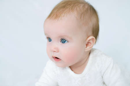 large portrait of little girl with blue eyes in white dress on white background, little girl looking at cameraの写真素材