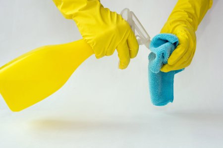 Female hands in yellow rubber gloves hold a spray for cleaning windows and cleaning cloth on a white...
