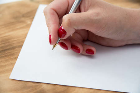 Womans hand with pen in position to write on blank white paper with room to add textの写真素材