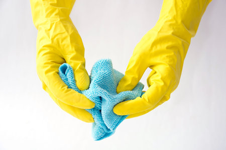 Closeup of a hand in a yellow latex glove using a blue towel to clean a counter top.
