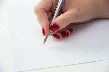 Womans hand with pen in position to write on blank white paper with room to add textの写真素材