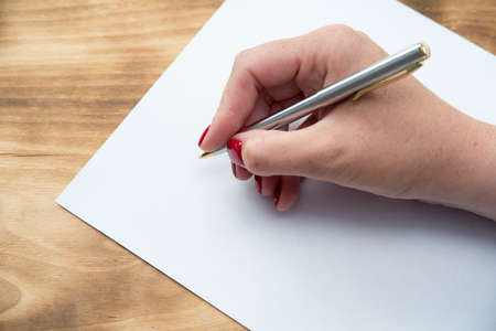Woman's hand with pen in position to write on blank white paper with room to add textの写真素材