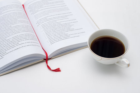 open book with red bookmark is next to a mug of black coffee white backgroundのeditorial素材