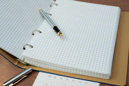 a silver fountain pen, a notebook with a blue cover and a calendar lie on a wooden tableの写真素材