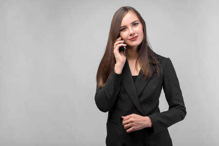 young beautiful girl in black business suit talking on the phone, white background, dark straight long hair, beautiful eyes, black jacketの写真素材