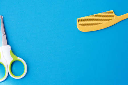 plastic yellow comb and green safety scissors for children, blue background top viewの写真素材
