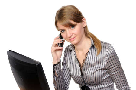 The beautiful smiling girl speaks by phone in front of her desktop computer on a white backgroundの写真素材