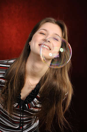 Young beautiful girl catch soap bubbles on red background の写真素材