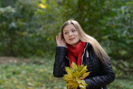 Young woman with autumn leaves in hand listening gossipの写真素材