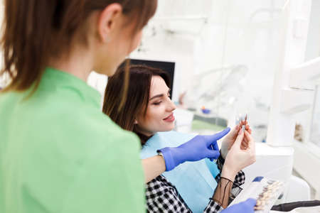 Dentist shows crown samples to his patient. Woman at the dentist's appointment chooses the tone of veneersの写真素材