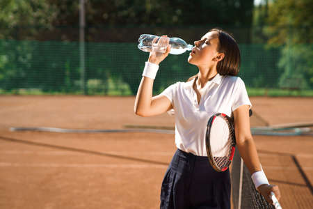 Young woman tennis player drinking waterの写真素材