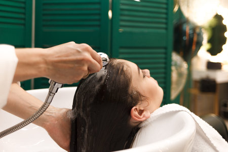 Beautiful young girl washes her head in a beauty studio. Hairdresser is washing hair for client