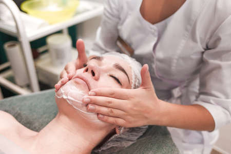Doctor beautician makes cosmetic facial massage. Woman relaxes on a cosmetic chairの写真素材