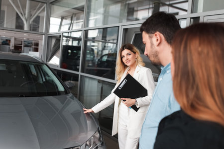 Car dealership manager shows cars to a young family couple