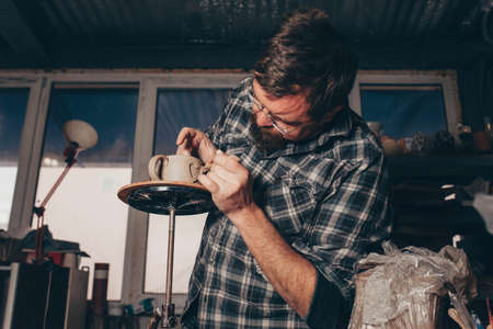 Bearded man works in a pottery workshop, concentrating on the process of creating a clay cupの写真素材