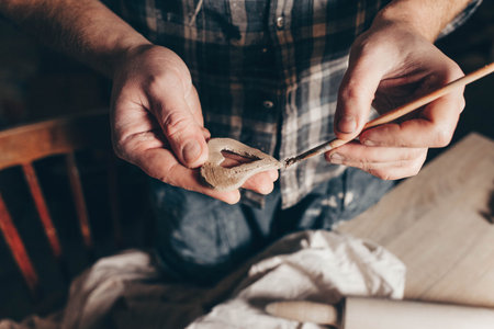 Ceramic master smears a heart cut out of clay with a brush