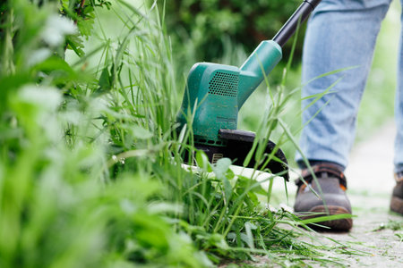 Man mows tall grass with an electric trimmer. Yard care concept