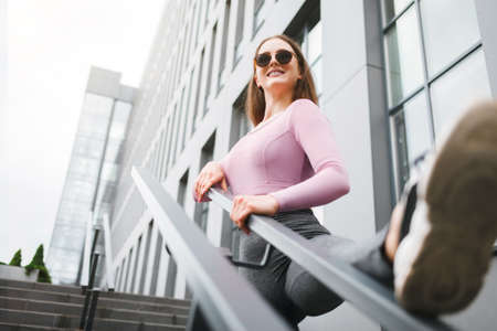 Smiling fitness woman doing workout. Girl is stretched on the stairsの写真素材