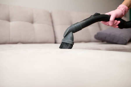 close up of woman's hand cleaning couch using vacuum cleaner at home sofa