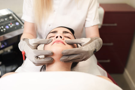 Doctor cosmetologist does facial massage to the patient with electric gloves