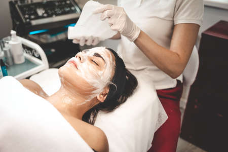 Cosmetologist washes off the mask from the patient's face. Removing a moisturizing mask from the faceの写真素材