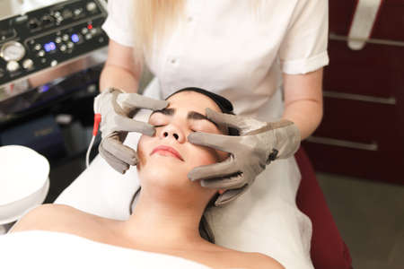 Doctor cosmetologist does facial massage to the patient with electric glovesの写真素材